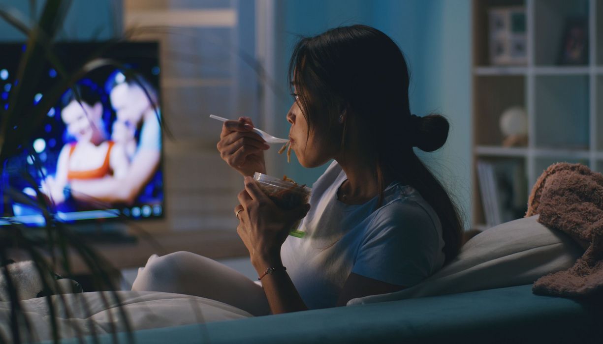 Frau sitzt im Dunkeln vor dem Fernseher und isst.