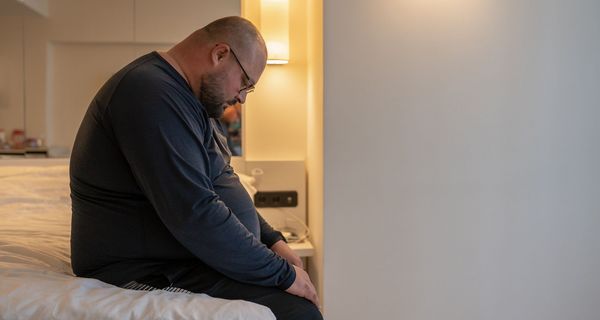 Stark übergewichtiger Mann, sitzt auf einem Bett.