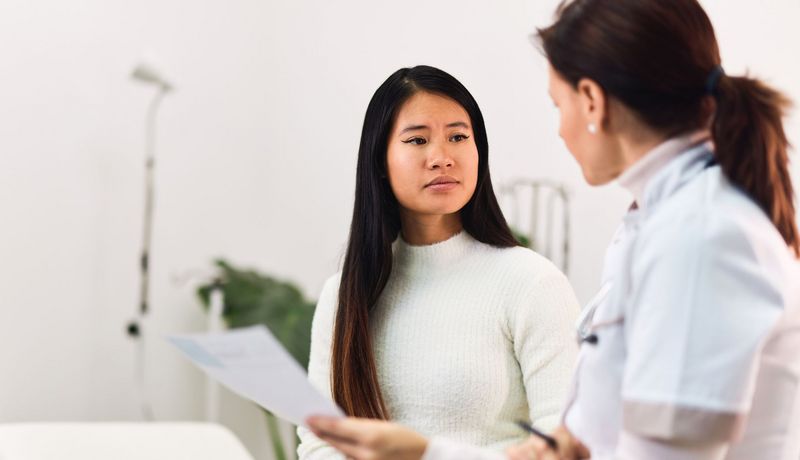 Ärztin hält ihrer Patientin einen Papierbogen hin und spricht mit ihr.