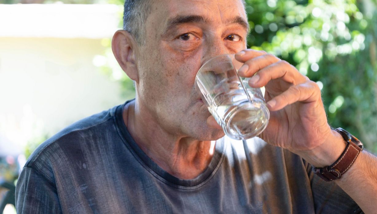 Senior, trinkt ein Glas Wasser.