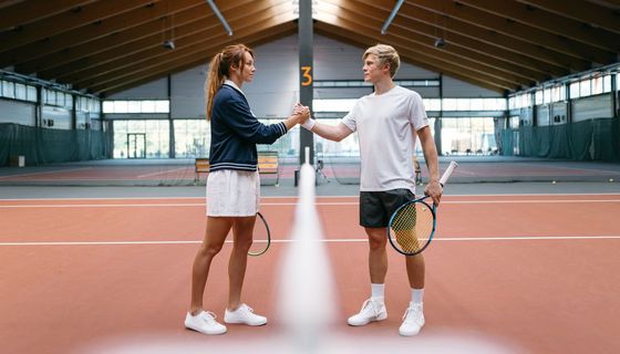 Zwei Tennisspieler geben sich die Hand am Netz.