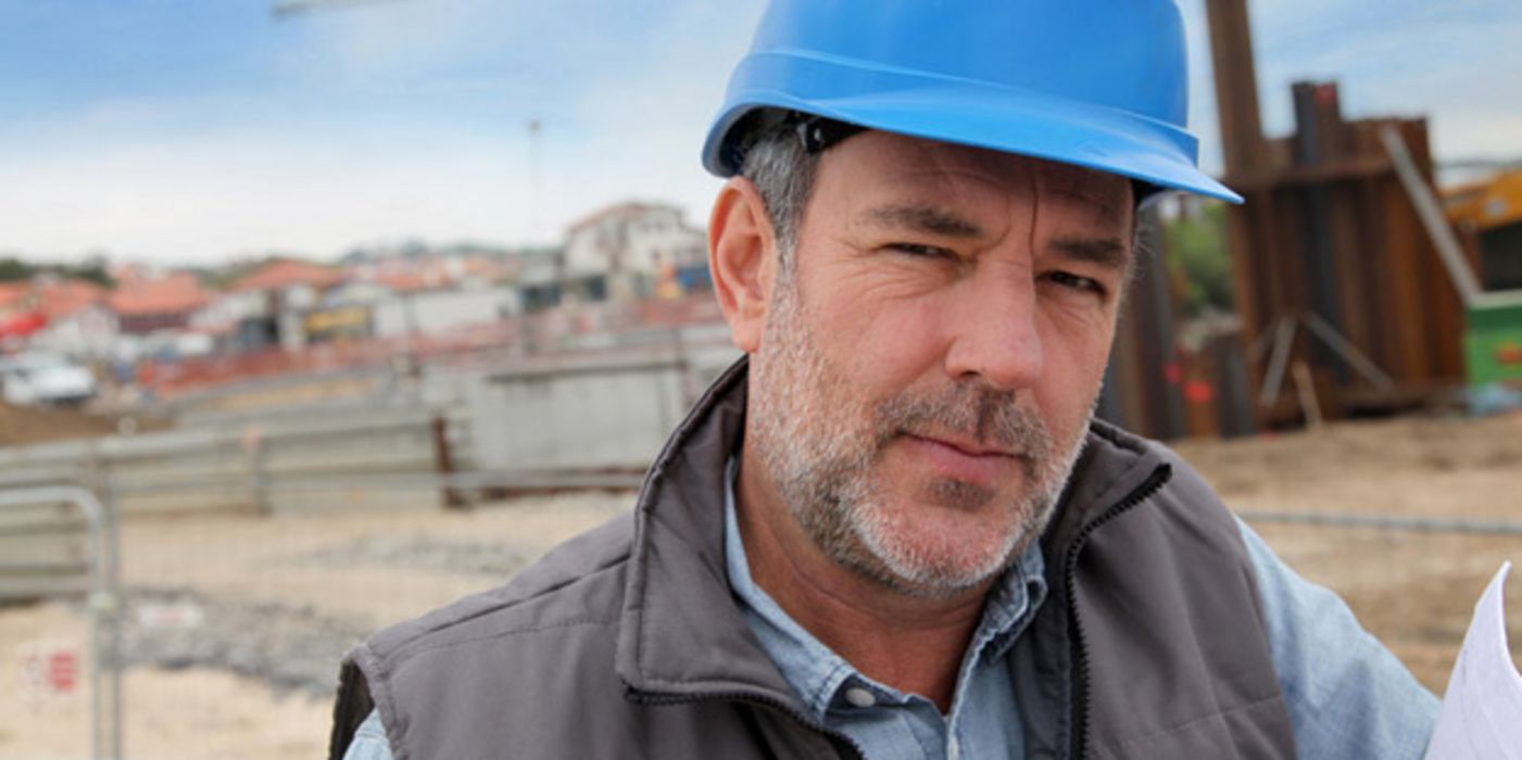 Mittelalter Bauarbeiter mit blauem Helm und Karohemd schaut in die Kamera