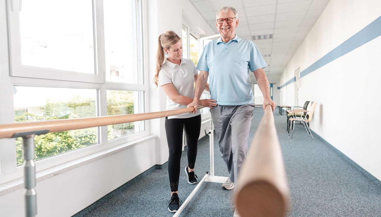 Physiotherapeutin hilft älterem Mann bei Übungen.