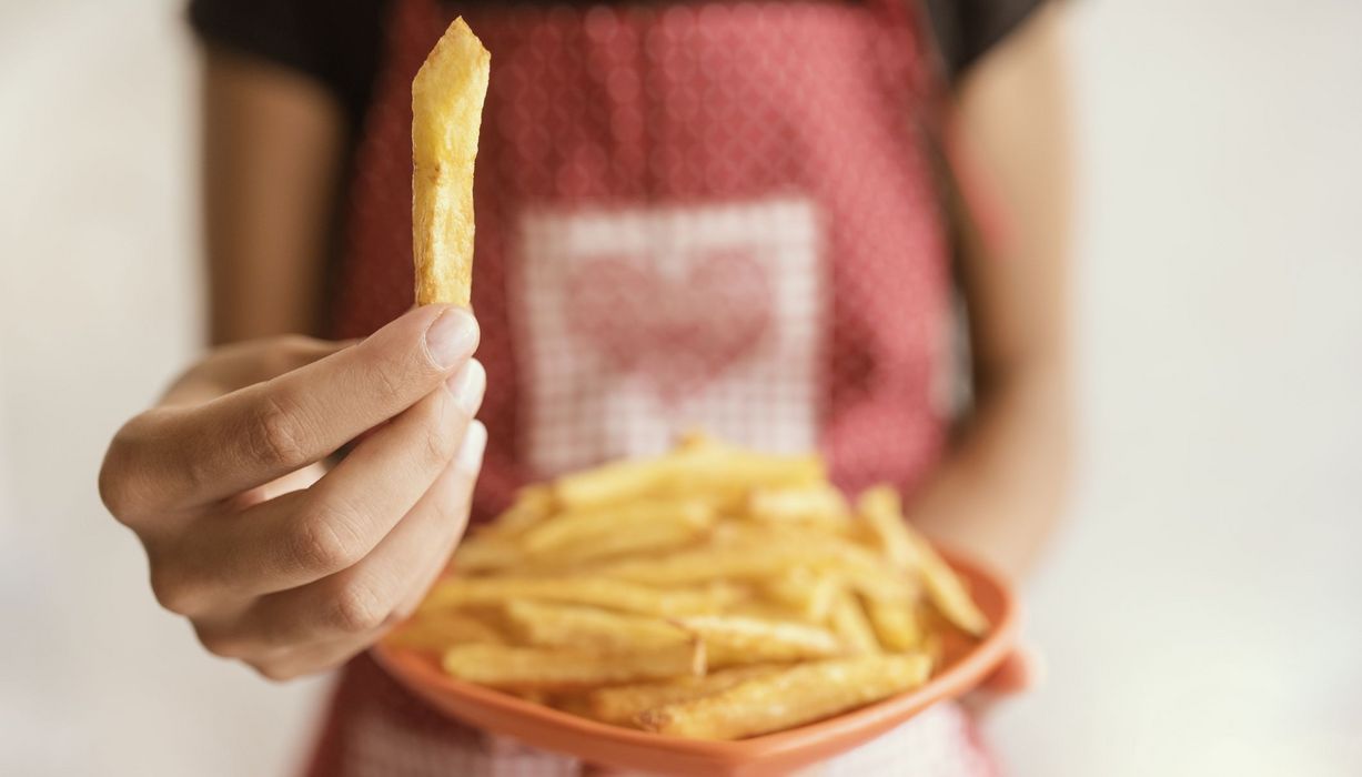 Frau mit einem Teller Pommes, hält eine Pommes in die Kamera.