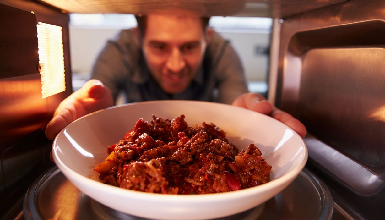 Mann, nimmt einen Teller mit Essen aus der Mikrowelle.