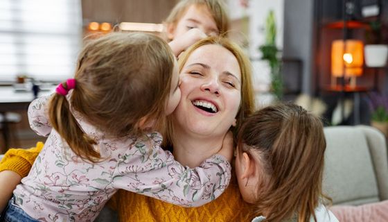Drei kleine Kinder kuscheln sich um eine glücklich aussehende, junge Frau.