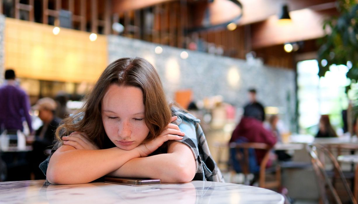 Jugendliches Mädchen, lehnt sich müde auf einen Tisch.