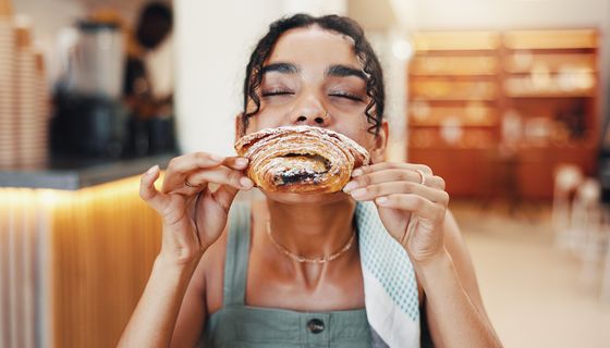 Eine junde FRau beißt genussvoll in ein süßes Gebäck.