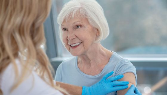 Krankenschwester klebt einer älteren Dame ein Pflaster auf den Link Oberarm - wohl nach einer Impfung.