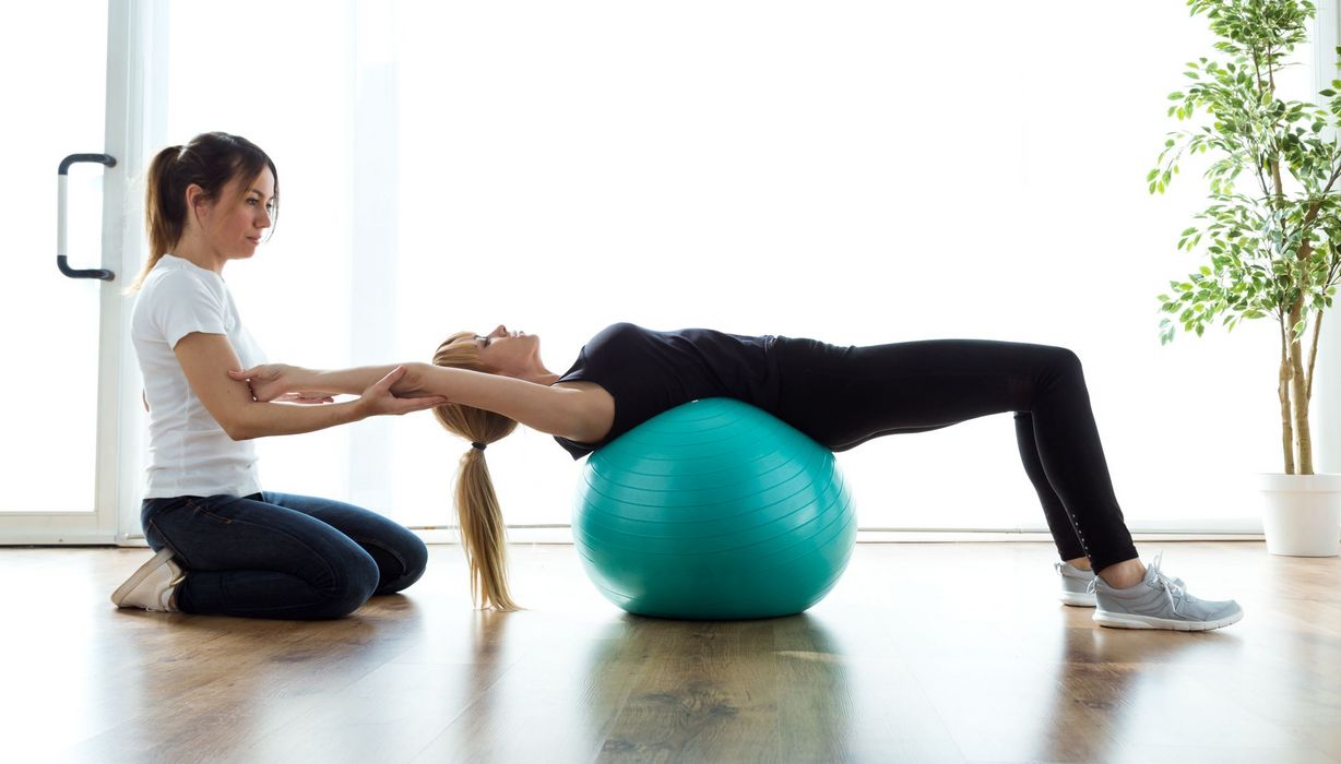 Schmerztherapeutin mit Patientin, macht Übungen mit einem Gymnastikball.