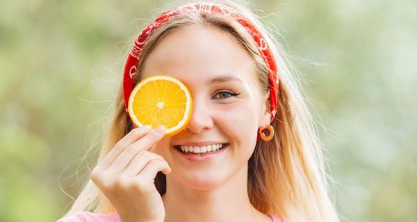 Junge Frau, hält sich eine Orangenscheibe vor das Auge und lacht.