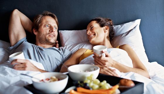 Ein Pärchen sitzt im Bett und frühstückt.