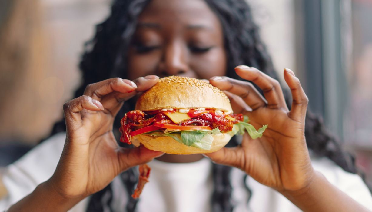 Frau, hält einen Hamburger in die Kamera.