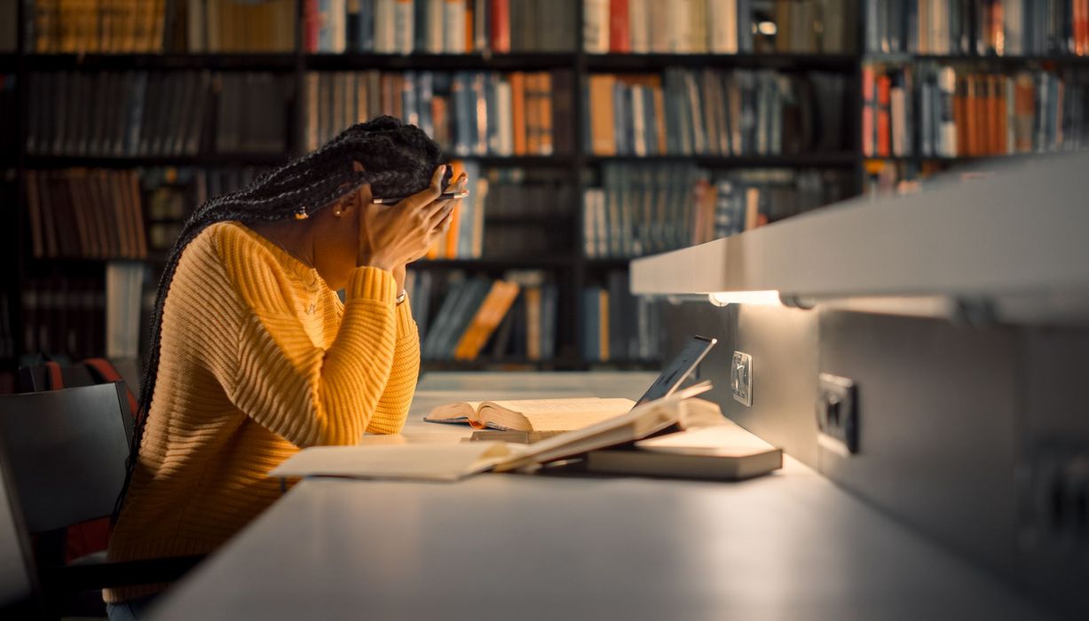 Frau, sitzt in der Bibliothek am Abend und stützt den Kopf in die Hände.