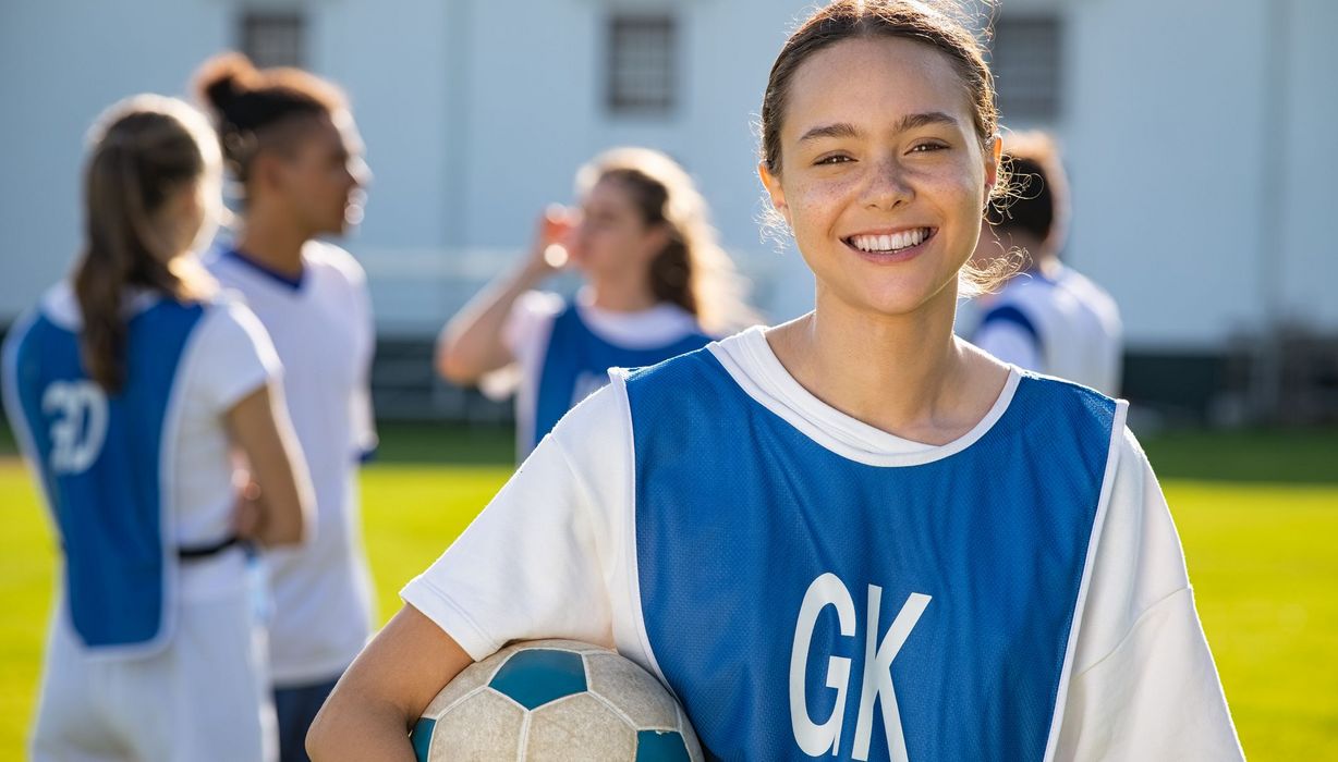 Junges Mädchen mit Fußball, lächelt in die Kamera.