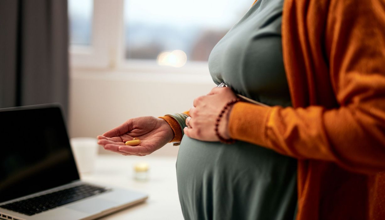 Schwangere Frau hält Nahrungsergänzungsmittel in der Hand.