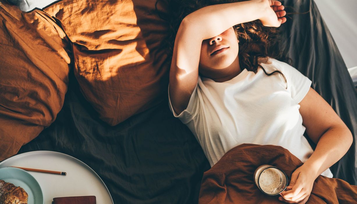 Frau, liegt im Bett mit einer Tasse Kaffee.