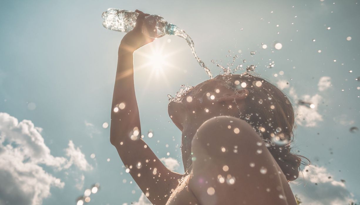 Frau, schüttet sich an einem sonnigen Tag Wasser über ihr Gesicht.