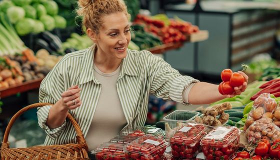 Frau beim Lebensmitteleinkauf: Sie hält lächelnd Tomaten in der Hand.