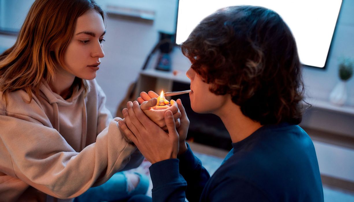 Zwei Jugendliche, Mädchen zündet Jungen einen Joint mit einem Feuerzeug ein.