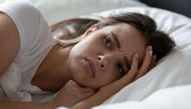 Junge Frau, liegt im Bett und macht sich Sorgen.