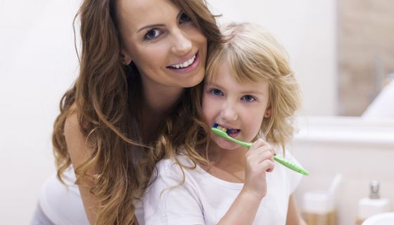 Mutter steht mit kleinem Mädchen vor dem Badezimmerspiegel und das Kind putzt sich die Zähne.
