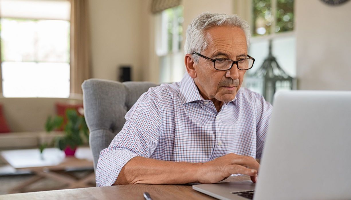 Senior sitzt vor dem Laptop.