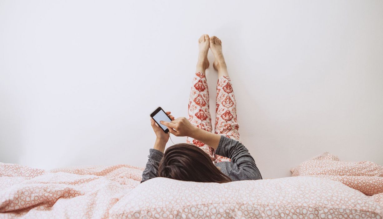 Junges Mädchen, liegt mit Smartphone im Bett.