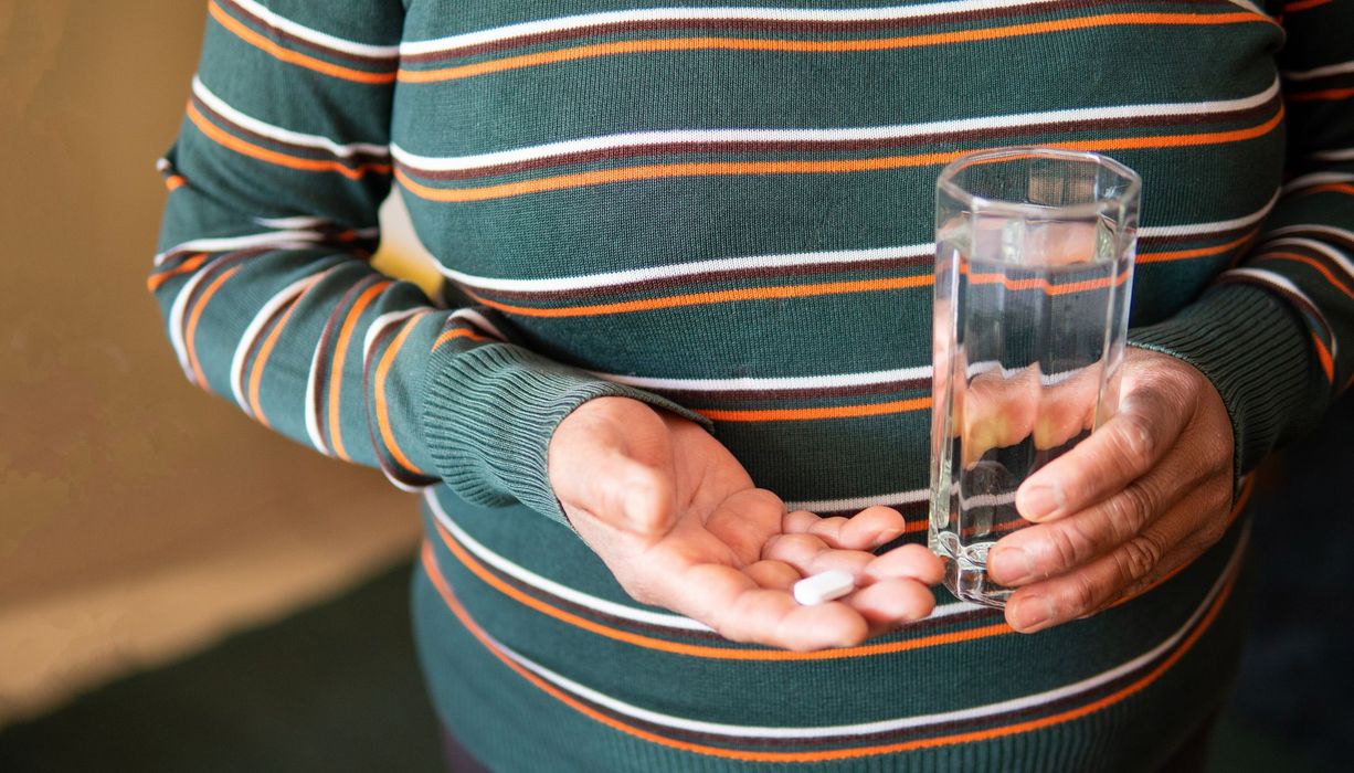 Übergewichtige Frau, hält eine Tablette und ein Glas Wasser in der Hand.