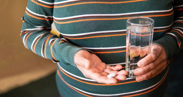 Übergewichtige Frau, hält eine Tablette und ein Glas Wasser in der Hand.