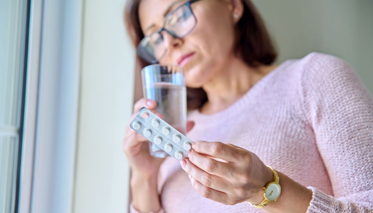 Frau, schaut skeptisch auf einen Blister mit Tabletten.