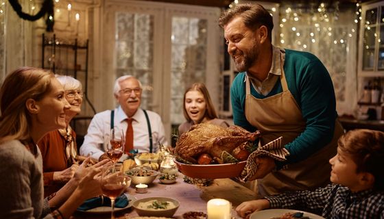 Eine Familie sitzt um den Weihnachtstisch herum. Ein Mann serviert eine große Gans