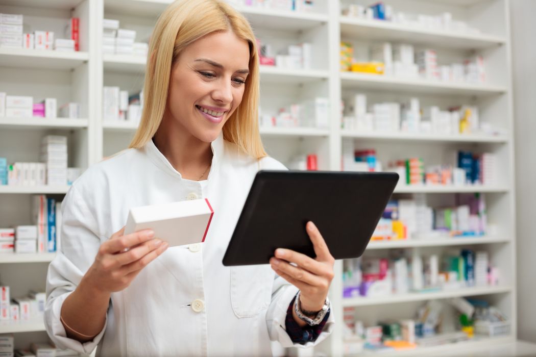 Apothekerin, hält ein Medikament und ein Tablet in der Hand.