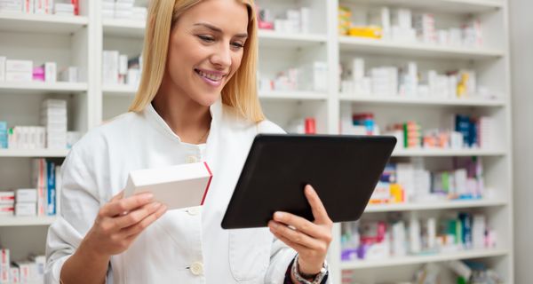 Apothekerin, hält ein Medikament und ein Tablet in der Hand.