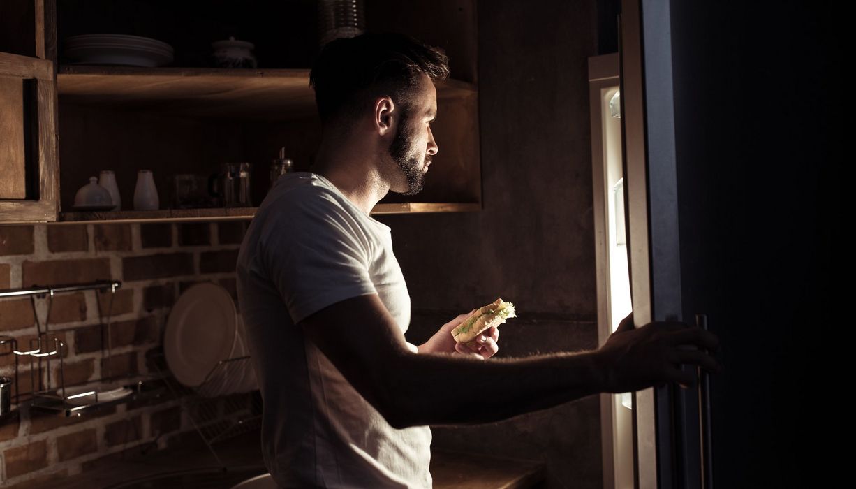 Junger Mann, schaut nachts in den Kühlschrank.