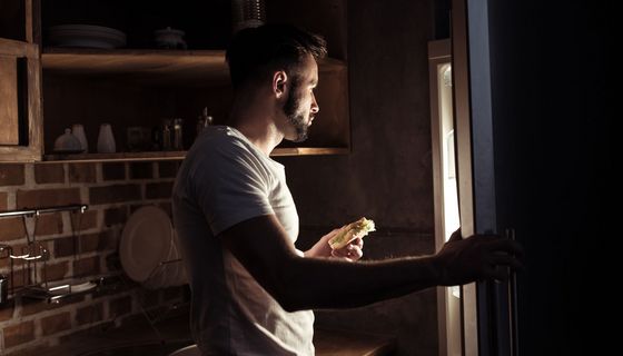 Junger Mann, schaut nachts in den Kühlschrank.