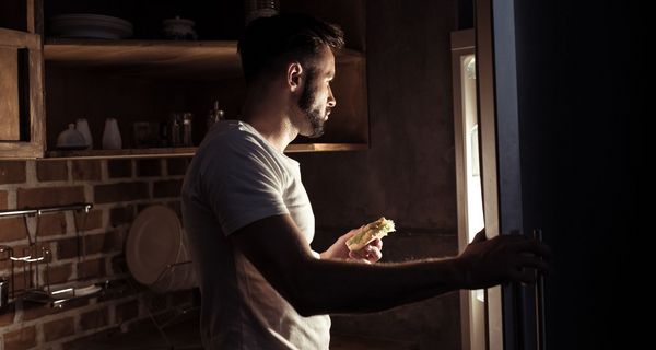 Junger Mann, schaut nachts in den Kühlschrank.