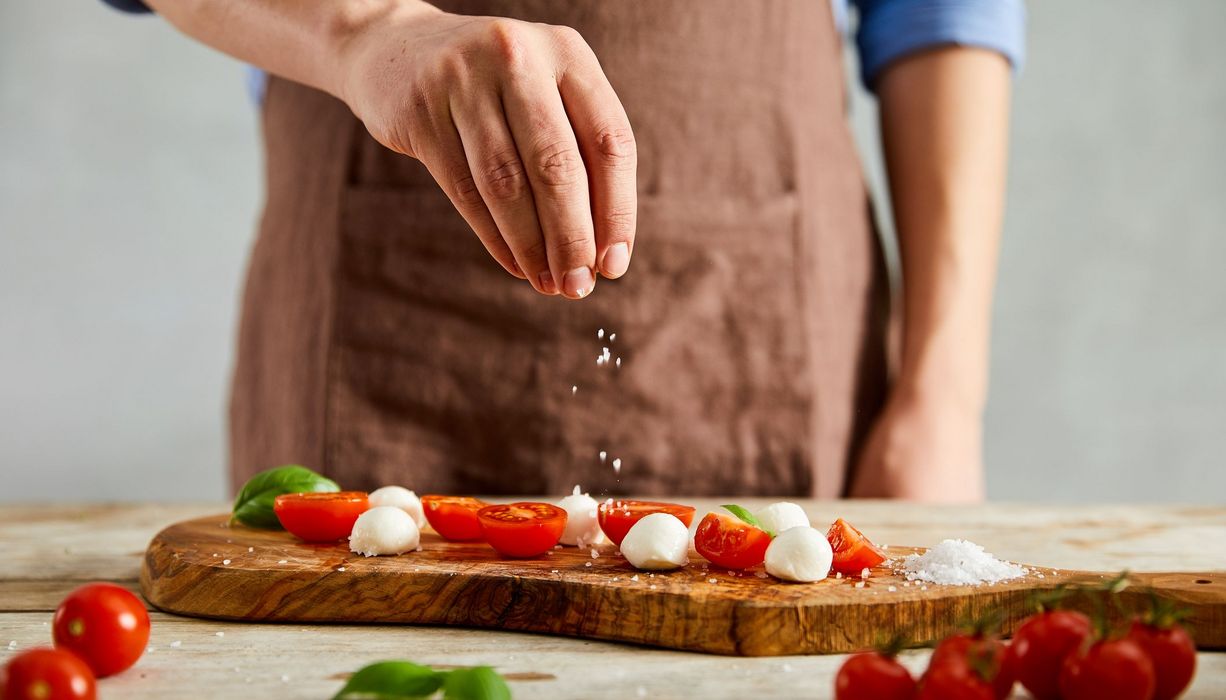 Mann, salzt Tomaten-Mozzarella-Salat.