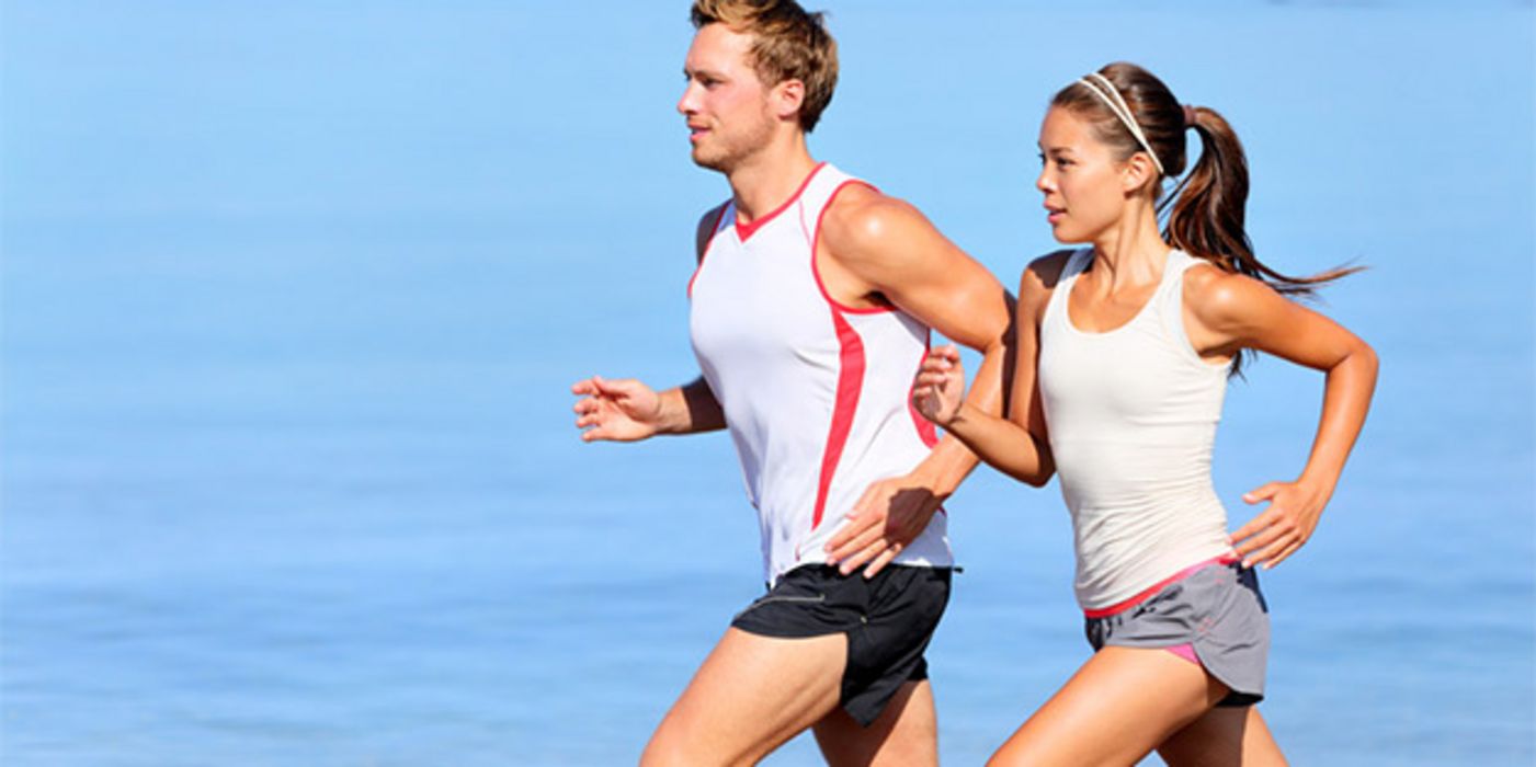 Frau und Mann um die 30, Profilbild, rechts, laufen in leichter Sportkleidung (Shorts, Sportshirts ohne Ärmel) schwitzend; Hintergrund Wasser