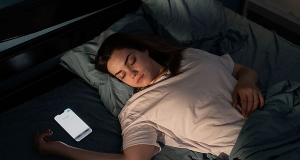 Teenagerin, liegt im Bett, neben ihr das Smartphone.