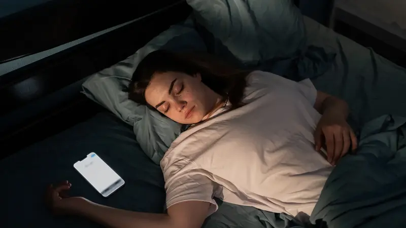 Teenagerin, liegt im Bett, neben ihr das Smartphone.