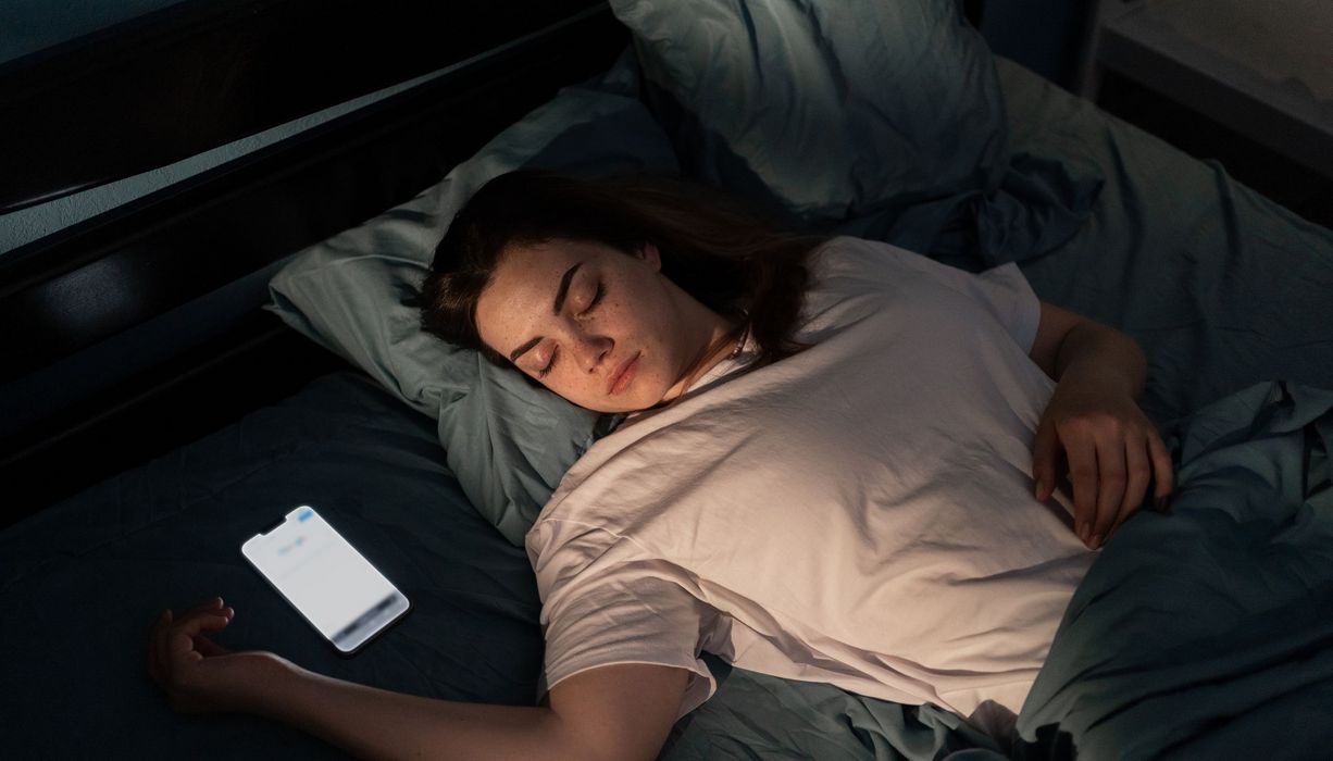 Teenagerin, liegt im Bett, neben ihr das Smartphone.