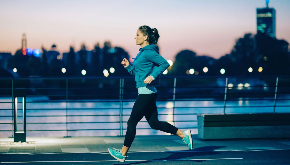 Junge Frau, joggt bei Dunkelheit in der Stadt.