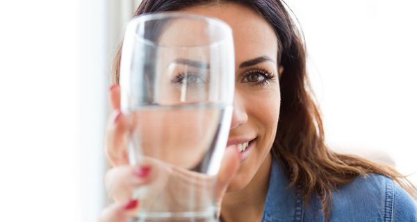 Junge Frau hält ein Glas Wasser dem Betrachter entgegen.