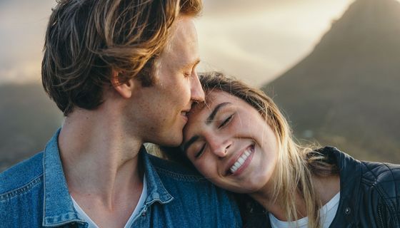 Selig lächelnde Frau legt den Kopf an die Schulter ihres Partenrs, der an ihrer Stirn lächelt.