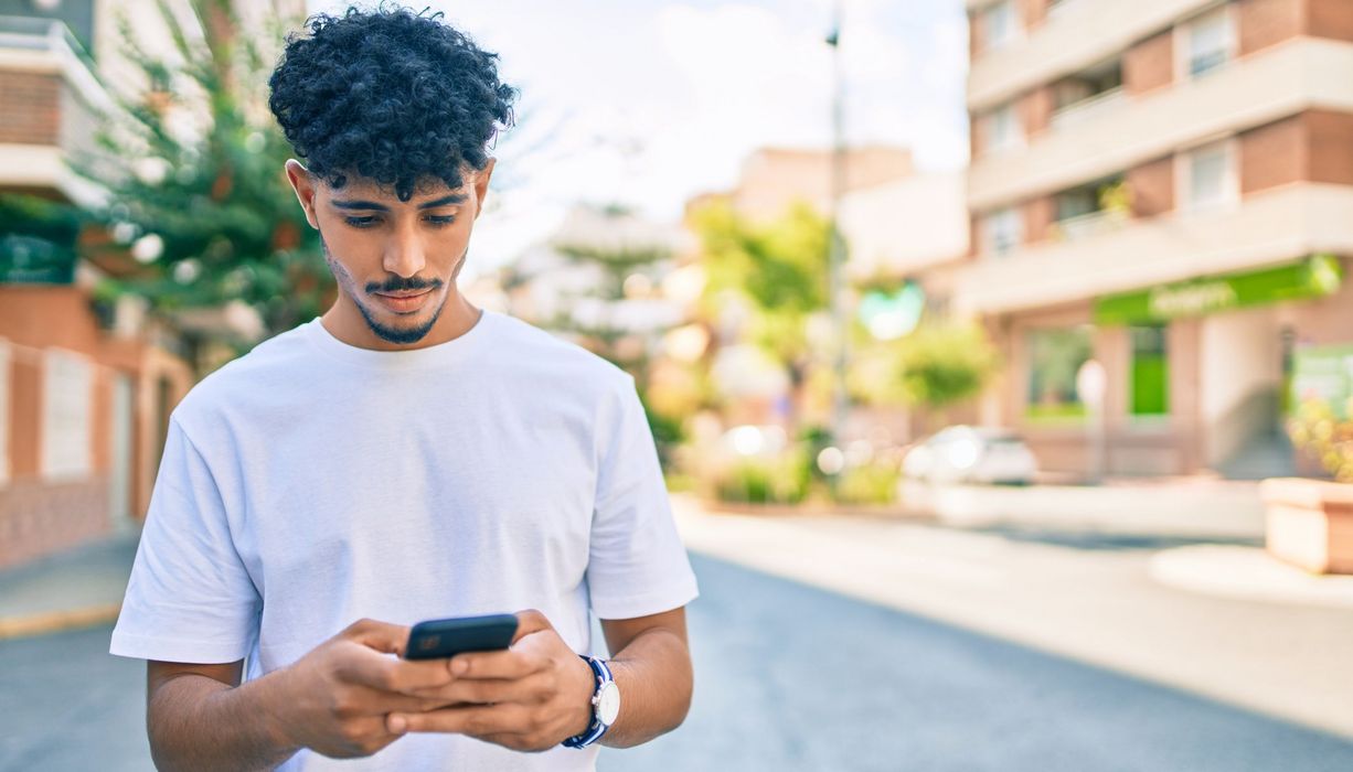 Junger Mann, schaut auf sein Smartphone.