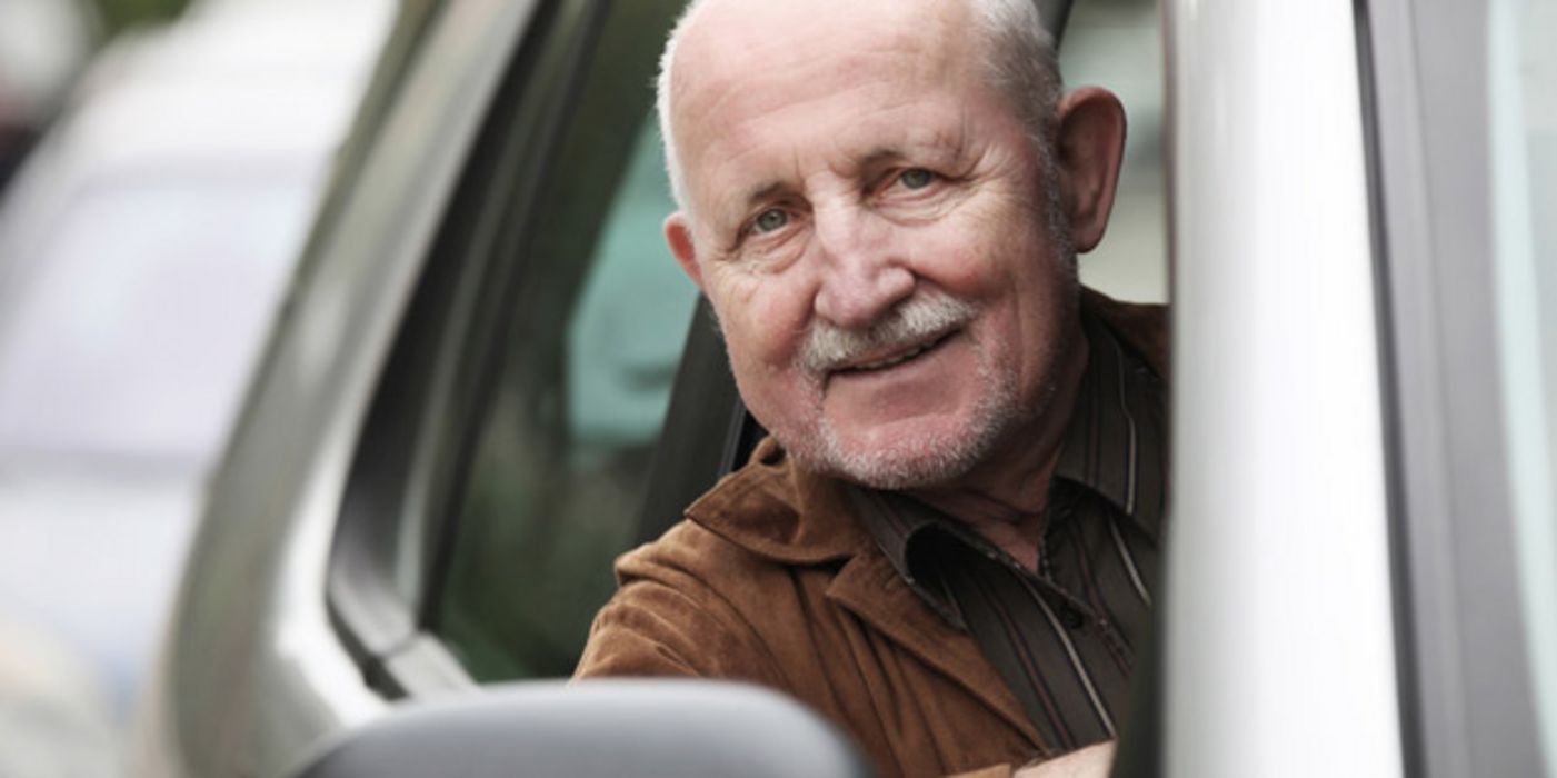 Älterer Mann sitzt im Auto und guckt aus dem Fahrerfenster