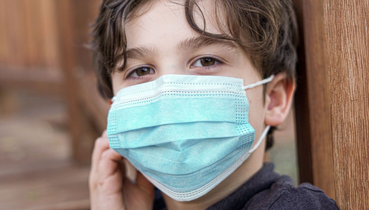 Junge mit braunen Haaren, trägt eine blaue OP-Maske.