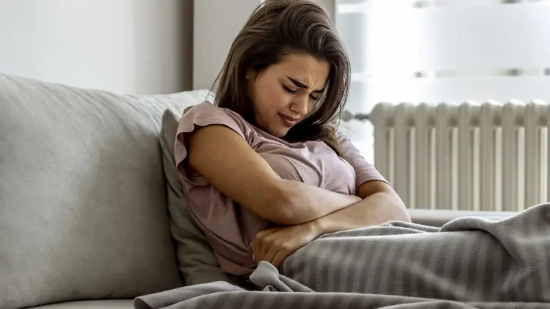 Junge Frau mit Bauchschmerzen, liegt im Bett.