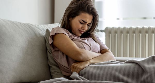 Junge Frau mit Bauchschmerzen, liegt im Bett.